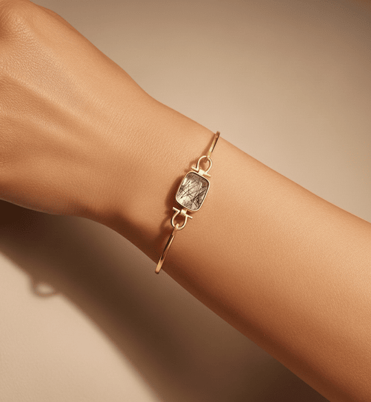 Silver gold plated bracelet with a stone on a wrist against a beige background