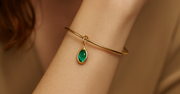 Silver with gold plated bracelet with a green gemstone on a person's wrist against a neutral background