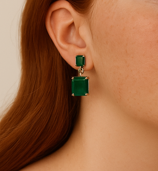 Green square earrings worn by a person with a neutral background
