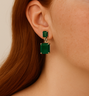 Green square earrings worn by a person with a neutral background